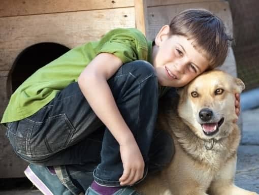 a boy crouched with his arm around his dog