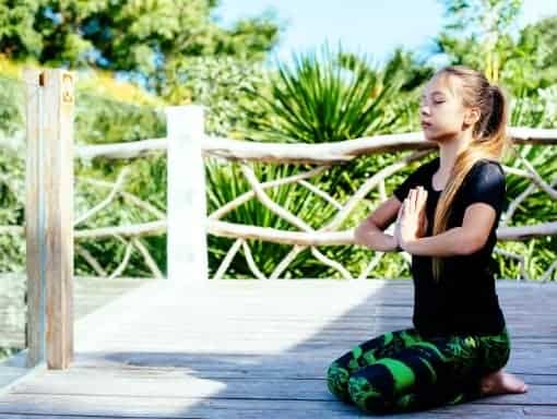 a girl kneeling on a wooden platform meditating outside