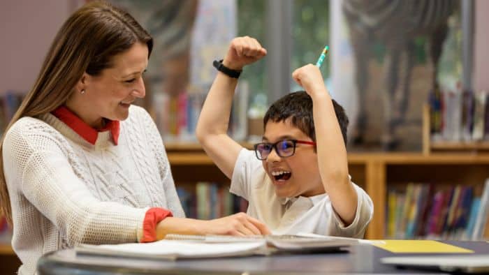 stock photo of tutor and primary child working in a library. Child is happy and punching the air