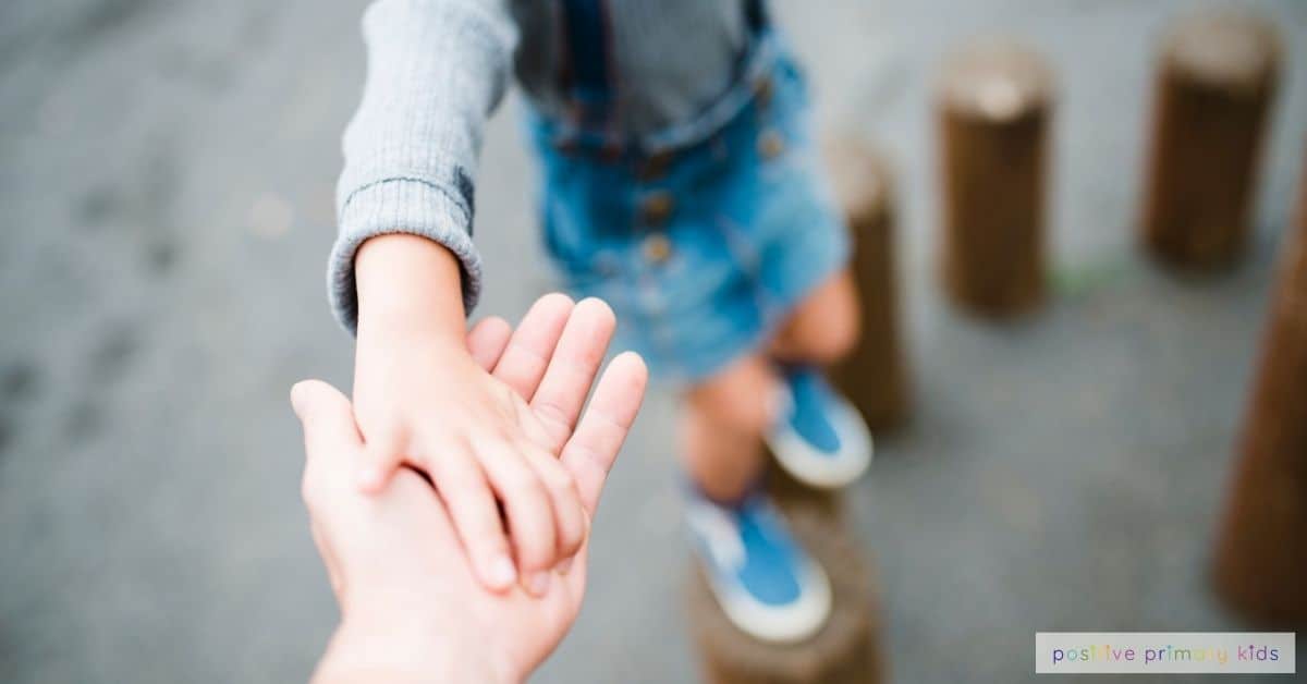 an adult hand in the foreground supporting a child in soft-focus who is balancing on tall playground equipment, showing focus and encouragement
